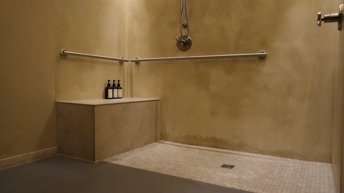 Curbless walk-in shower with grab bars, a built-in bench, and a mosaic tile floor
