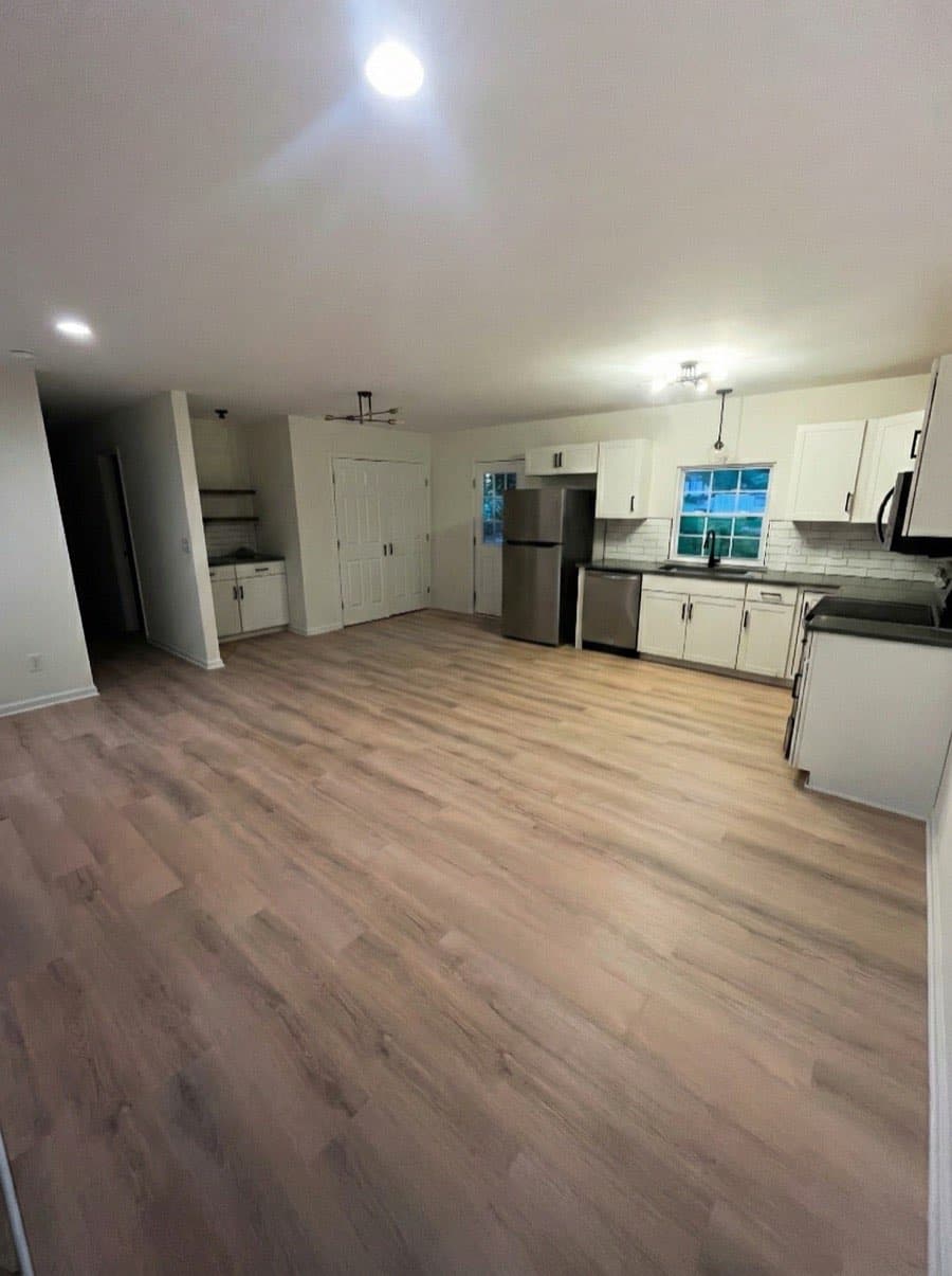 Open kitchen and living area with newly installed luxury vinyl plank flooring, white cabinets, and stainless appliances