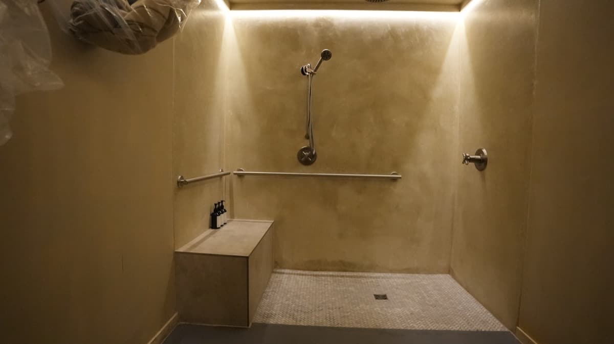Large walk-in shower with a corner bench, grab bar, and herringbone mosaic tile floor