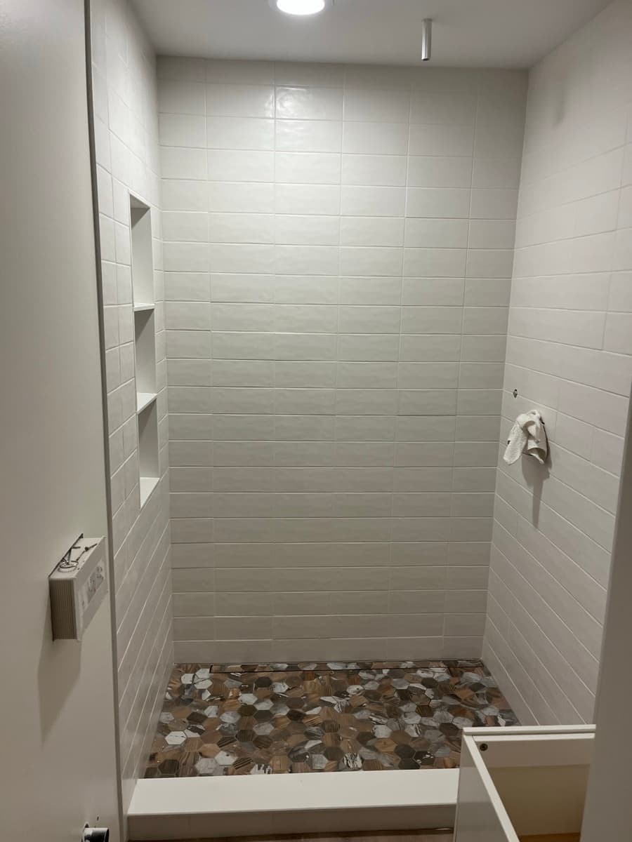 Walk-in shower with white subway wall tile, recessed shelf niche, and a mixed wood-look hexagon mosaic floor